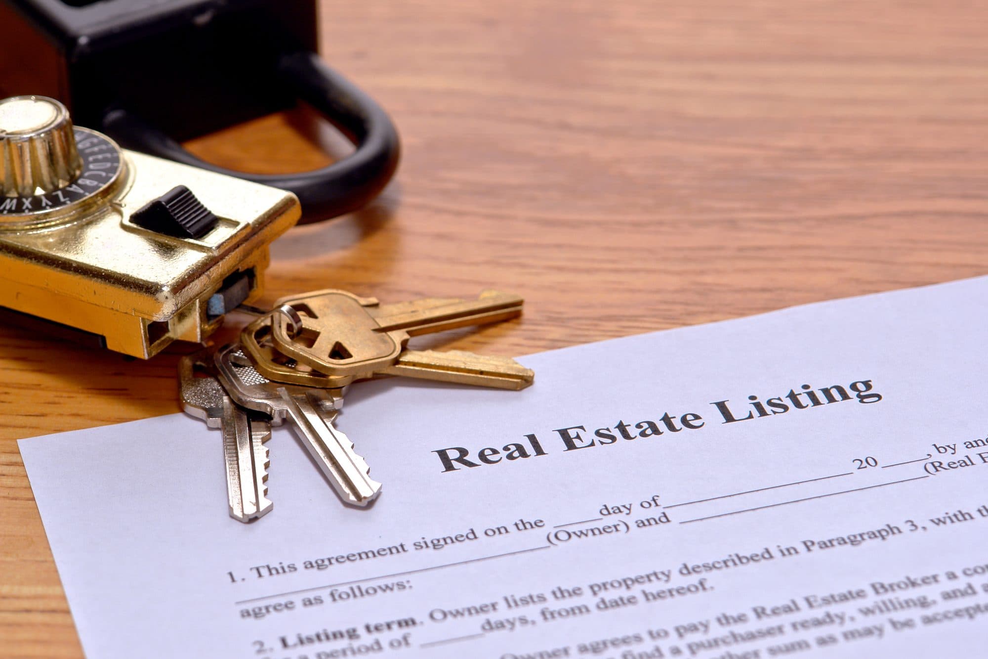 A listing agreement on a desk beside a set of house keys and a lockbox